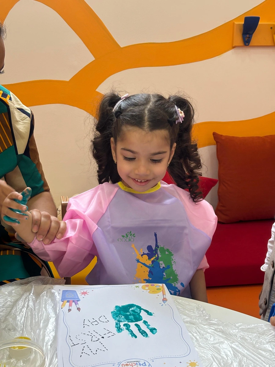 Une enfant réalise une empreinte de main en peinture avec l’aide d’une adulte chez Ptichou.