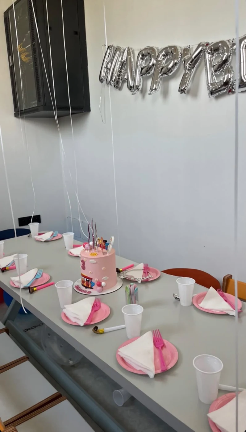 La table préparée pour un anniversaire chez Ptichou, avec le gâteau, les assiettes roses et les décorations de fête.